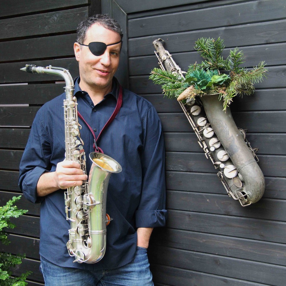 A man holding two saxophones in front of a wall.