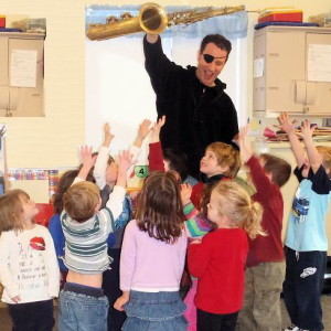 A man holding up a saxophone in front of children.